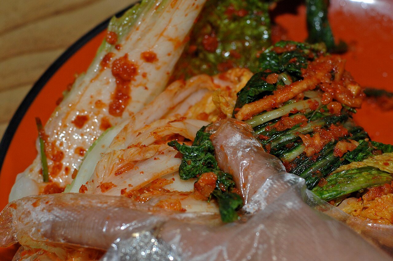 Hands rubbing red chili seasoning paste between the leaves of salted napa cabbage