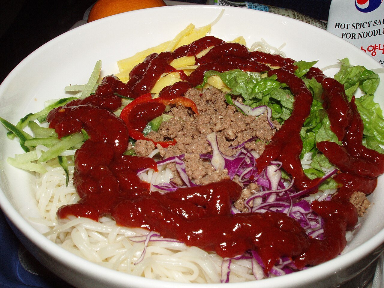 A bowl of bibim guksu, cold spicy noodles mixed with vegetables and a fried egg on top