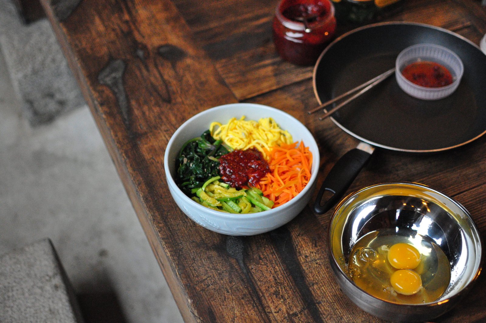 An unmixed bibimbap bowl with seasoned vegetables arranged in wedges around a fried egg