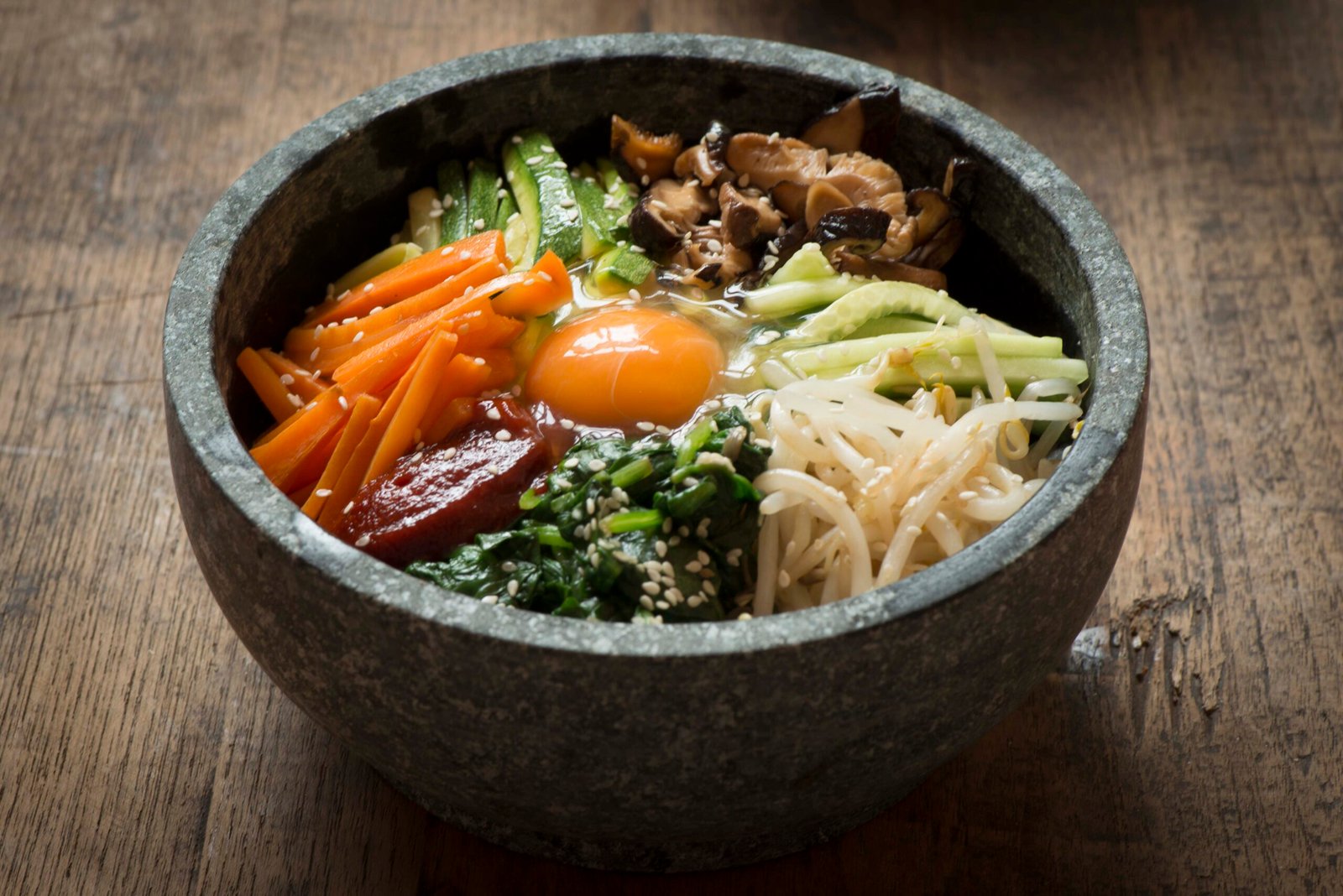 Dolsot bibimbap sizzling in a hot stone bowl with a raw egg yolk in the center