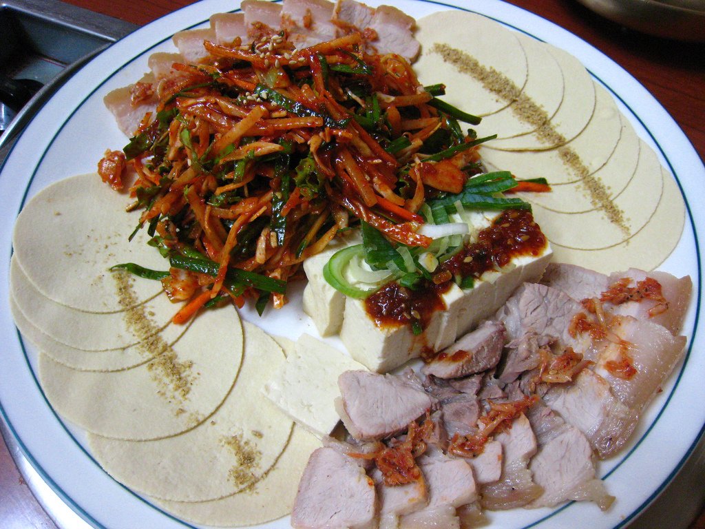 A bossam platter with thick-sliced pork, whole garlic cloves, chili, and ssamjang dip
