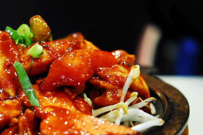A skillet of buldak, bite-sized chicken pieces coated in a glossy, deep red chili sauce with charred edges