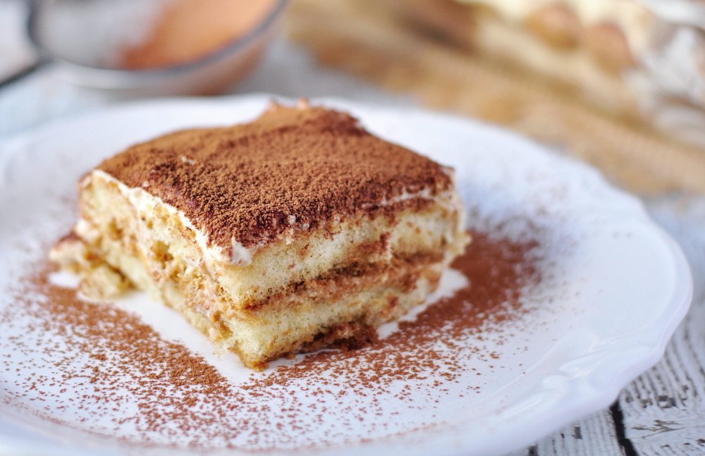 A square slice of layered tiramisu dusted with cocoa powder on a white plate