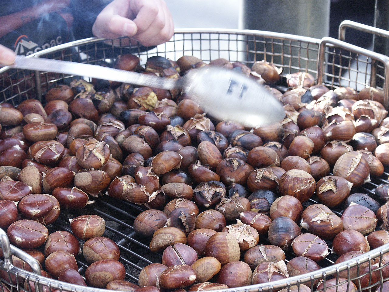A pile of roasted chestnuts, some split open, being sold at a street stall