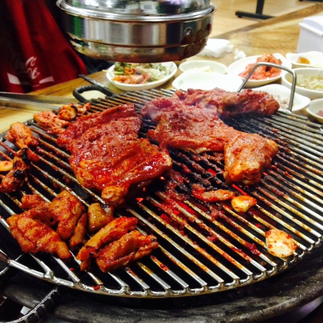 A large flat pan of Chuncheon-style dakgalbi with chicken, cabbage and rice cake cooking over a tabletop burner