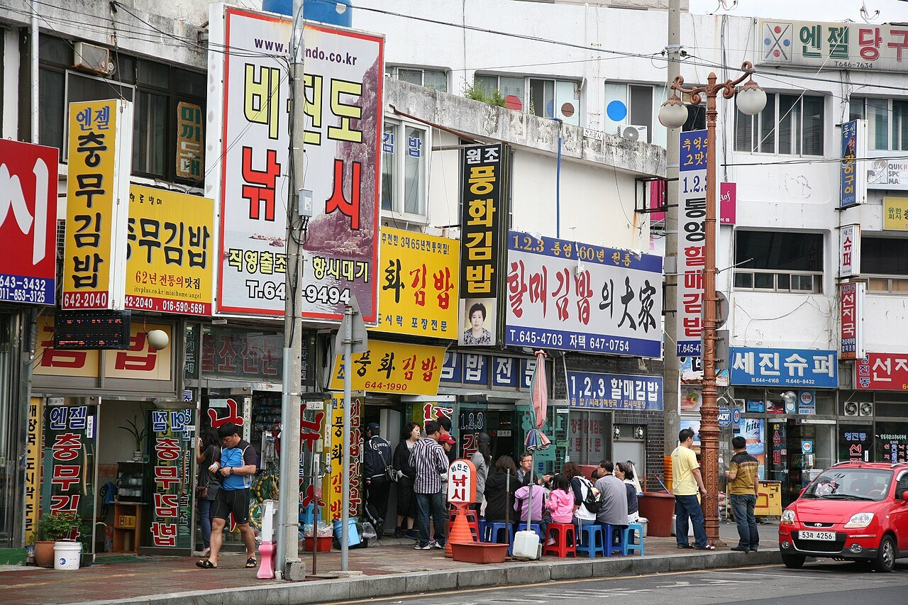 A street vendor's tray of chungmu gimbap rolls alongside small dishes of spicy squid and radish