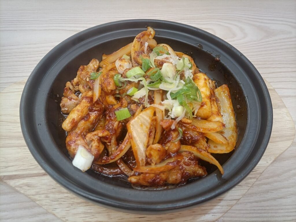 A wide iron pan of Chuncheon-style dakgalbi with red-sauced chicken, cabbage and rice cakes