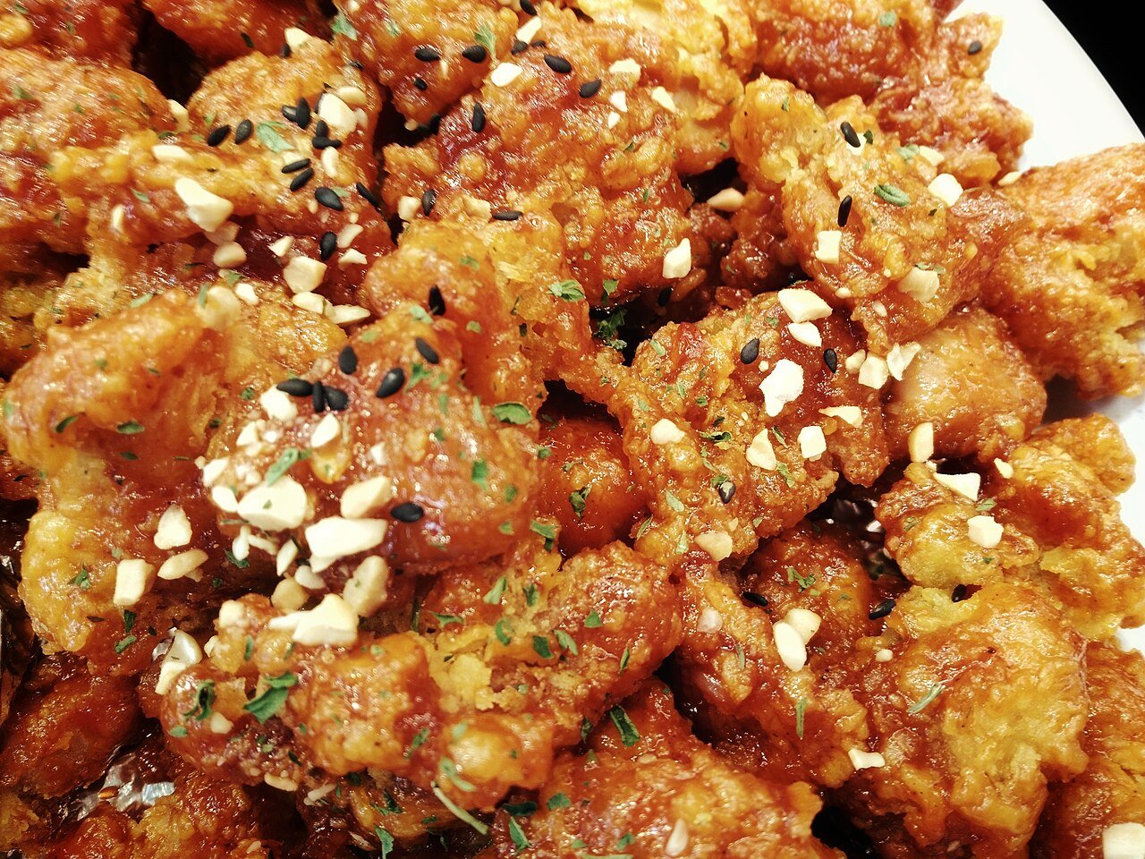A bowl of dakgangjeong, fried chicken pieces coated in a glossy, glass-like sweet glaze with sesame seeds and dried chili