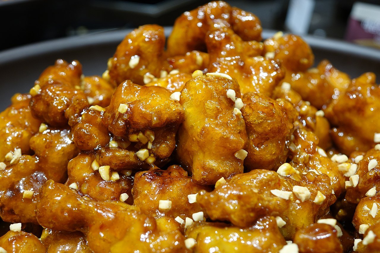 Close-up of small dakgangjeong chicken pieces with a hard, shiny glaze and scattered peanuts