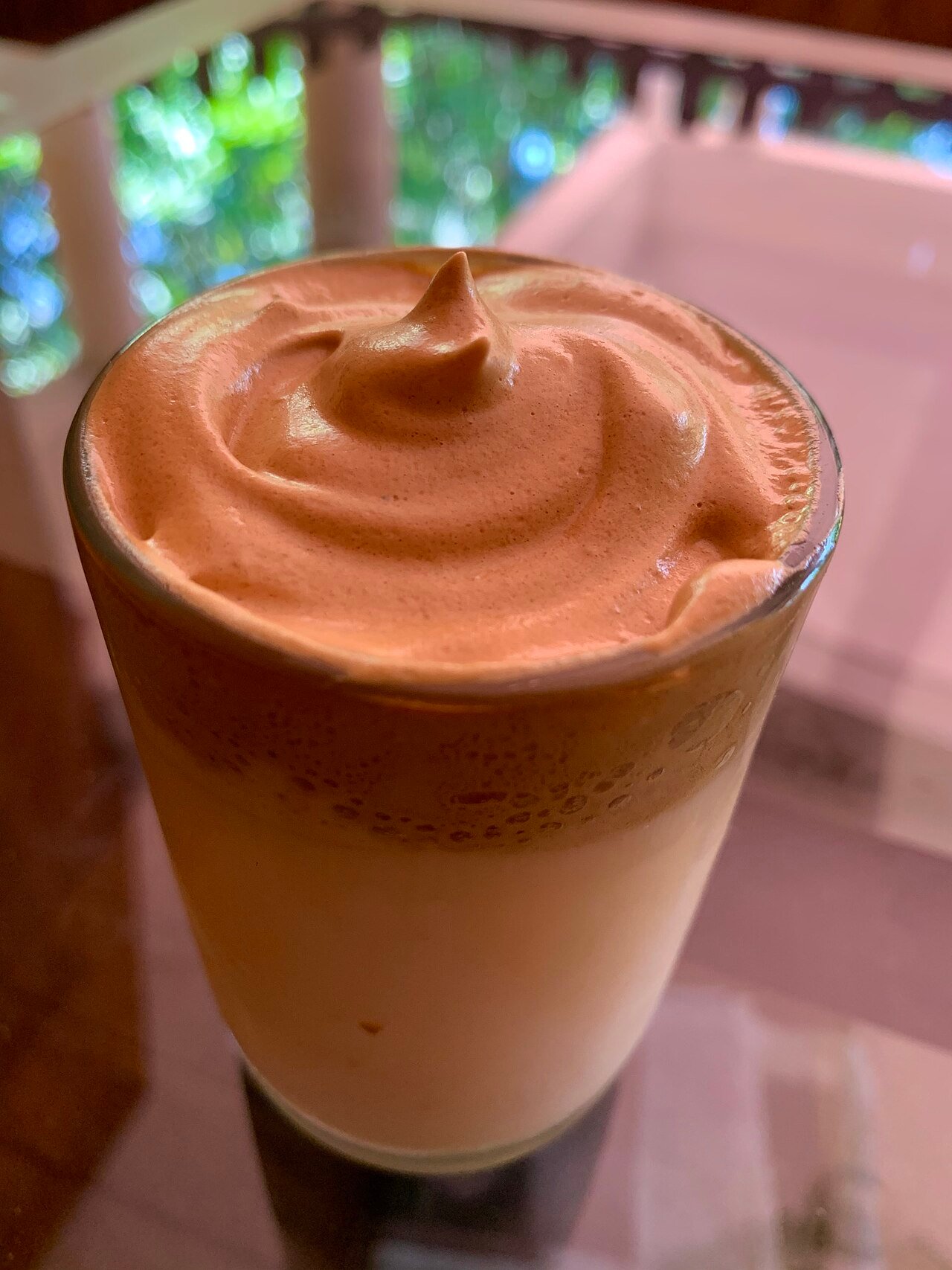 A homemade dalgona coffee drink showing whipped coffee foam layered over milk in a clear cup