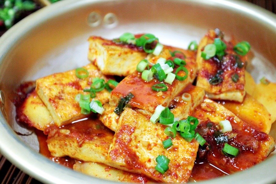 A bowl of braised tofu cubes glazed in a dark savory Korean sauce