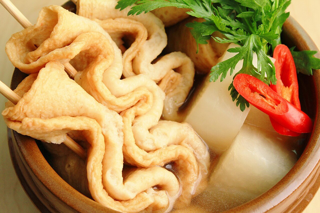 A close-up bowl of Korean fish cake soup with pleated fish cake skewers, radish, and sliced red chili in broth