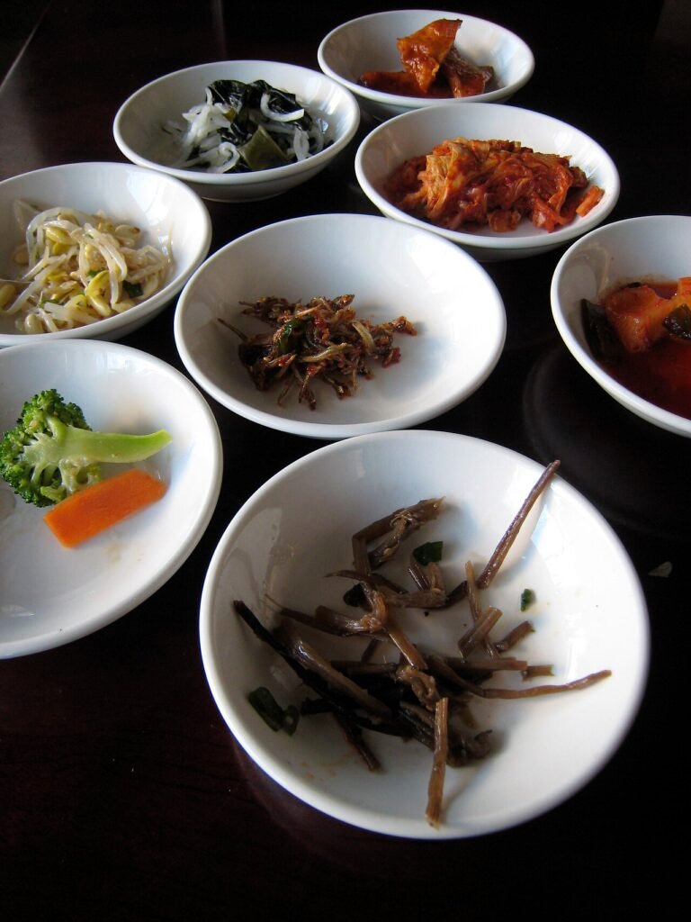 An assortment of small Korean side dishes, banchan, served in individual bowls around a table