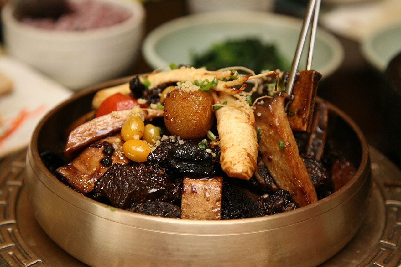 A close view of braised short ribs and vegetables in glossy soy sauce, showing the meat pulling away from the bone