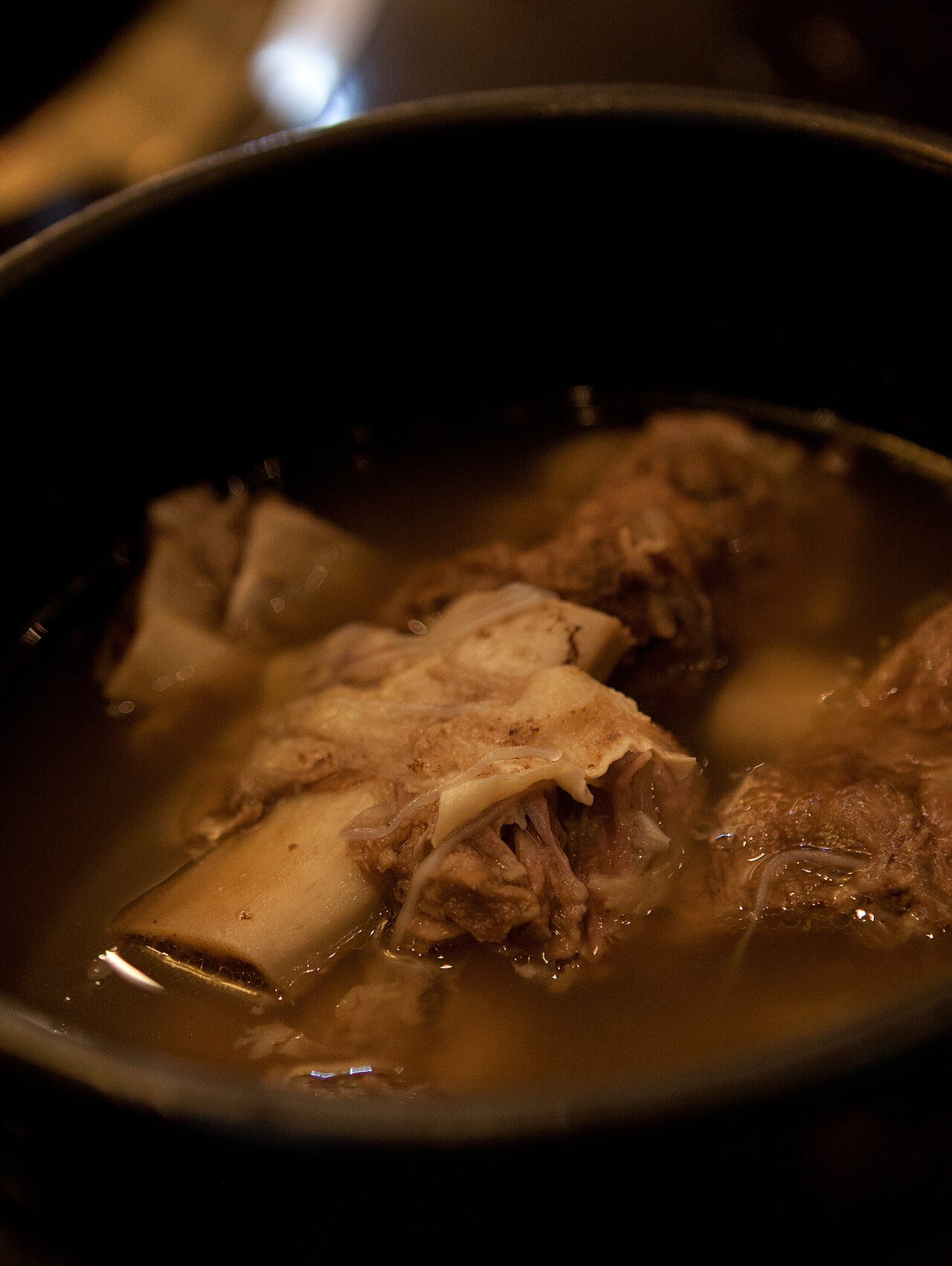 A bowl of clear galbitang broth with a short rib, glass noodles, and shredded egg garnish