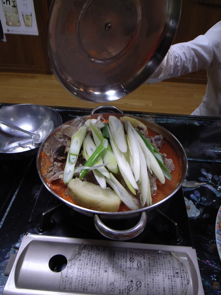 A dark red pot of gamjatang with pork bones, potatoes, and perilla leaves