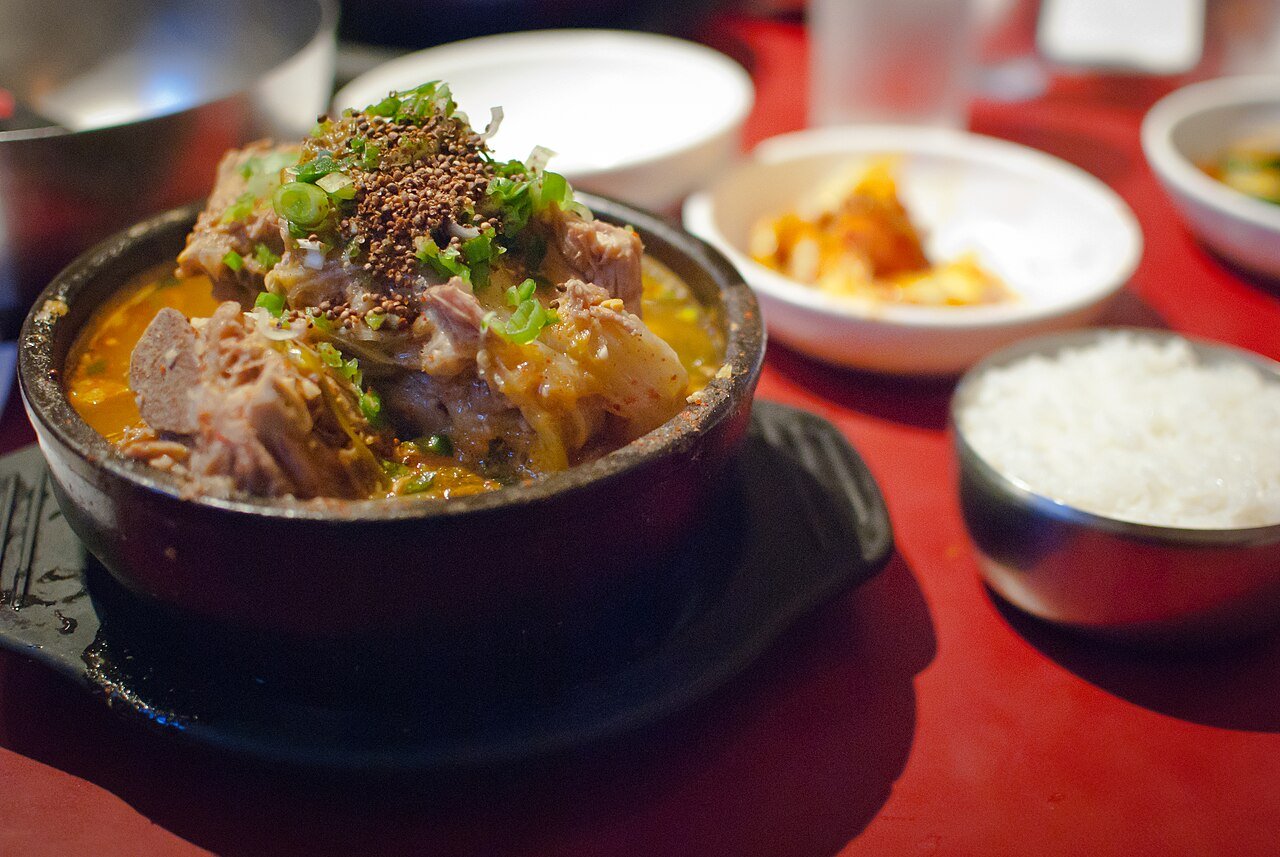Gamjatang served in a stone pot at a restaurant table with side dishes