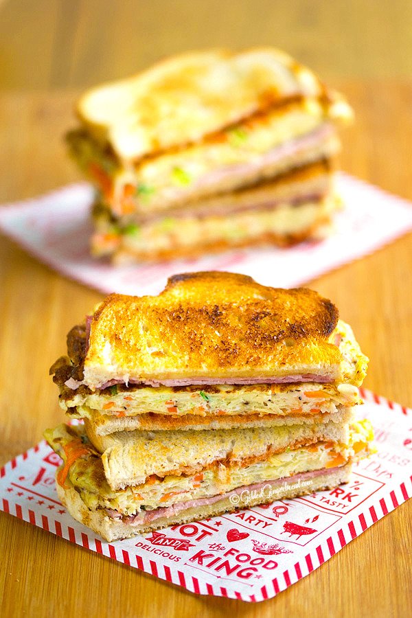 Close-up of Korean street toast cut in half, showing the layered cabbage egg patty, ham, and cheese