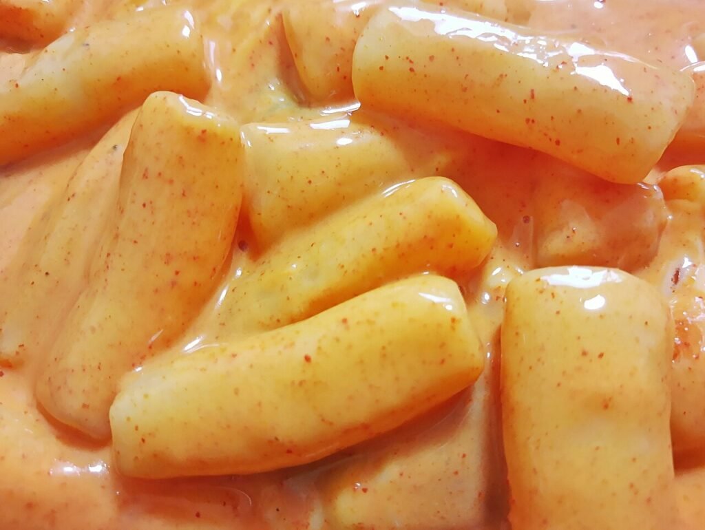 A home-cooked serving of rose tteokbokki, rice cakes coated in a creamy pink-orange gochujang-cream sauce