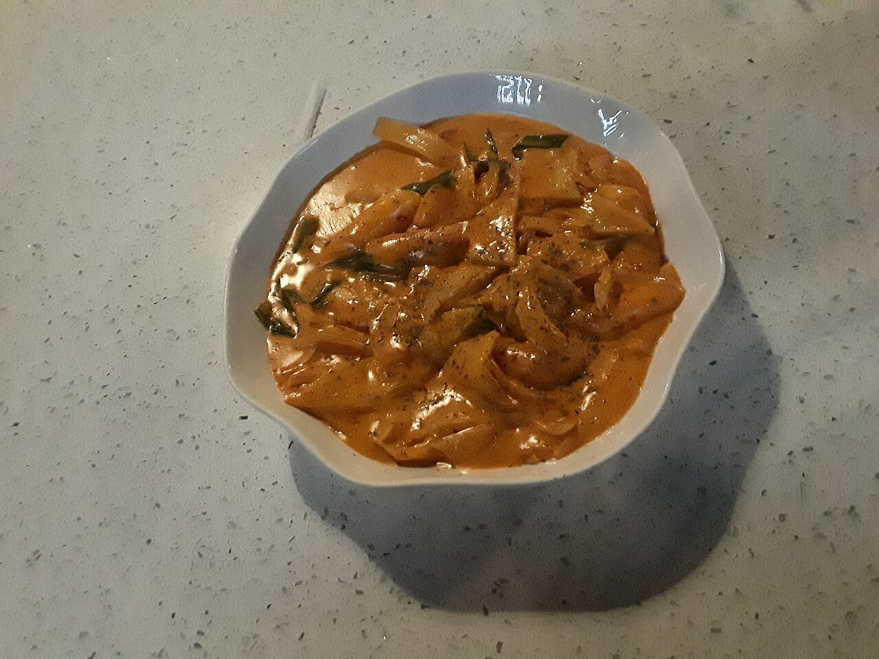 A plate of rose tteokbokki, rice cakes in a creamy pink-orange sauce, served at a Korean restaurant