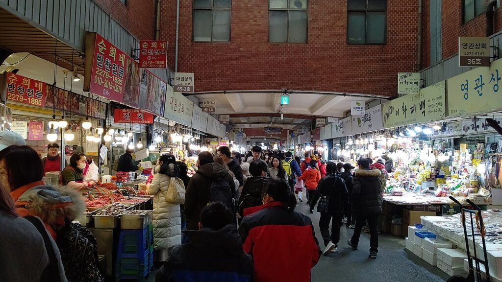 A busy covered aisle inside Gwangjang Market in Seoul lined with food stalls and customers on stools