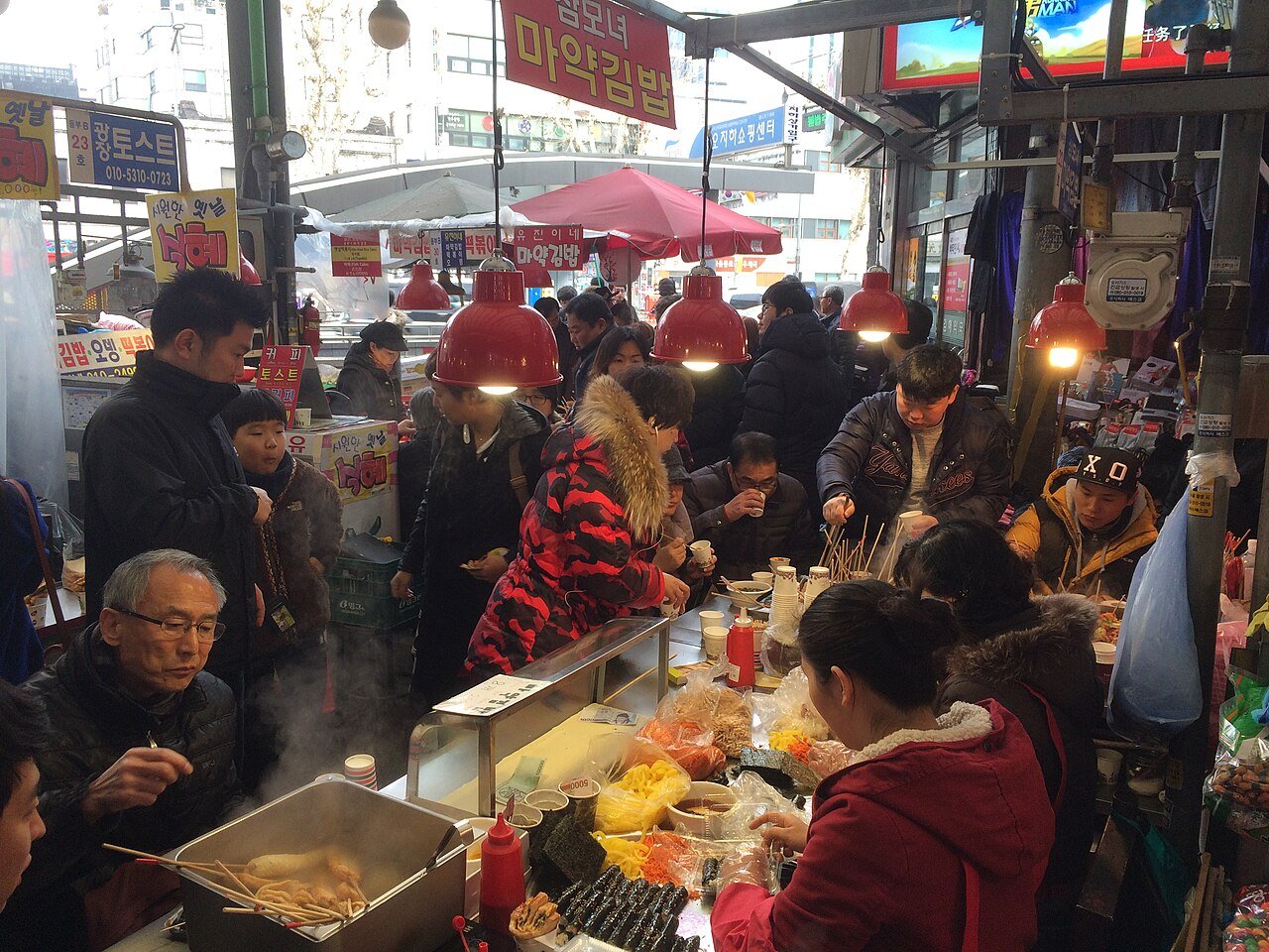 Vendors rolling trays of tiny mayak gimbap seaweed rice rolls at a Gwangjang Market stall