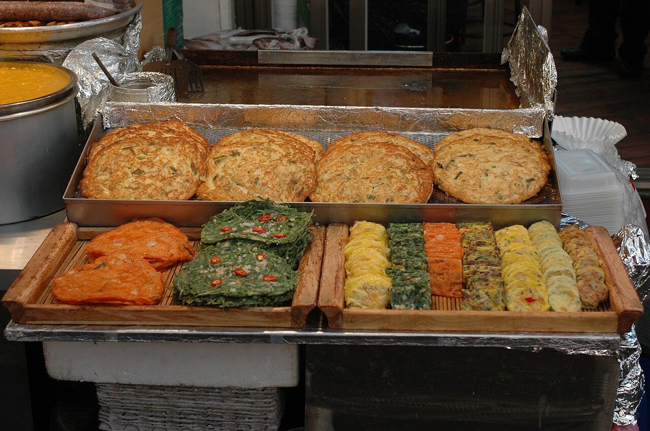Trays of Korean jeon pancakes and pan-fried vegetables and fish displayed along an alley at Gwangjang Market