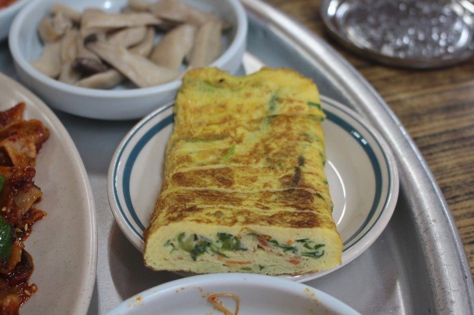 A rolled Korean egg omelette on a cutting board with a knife, sliced into rounds