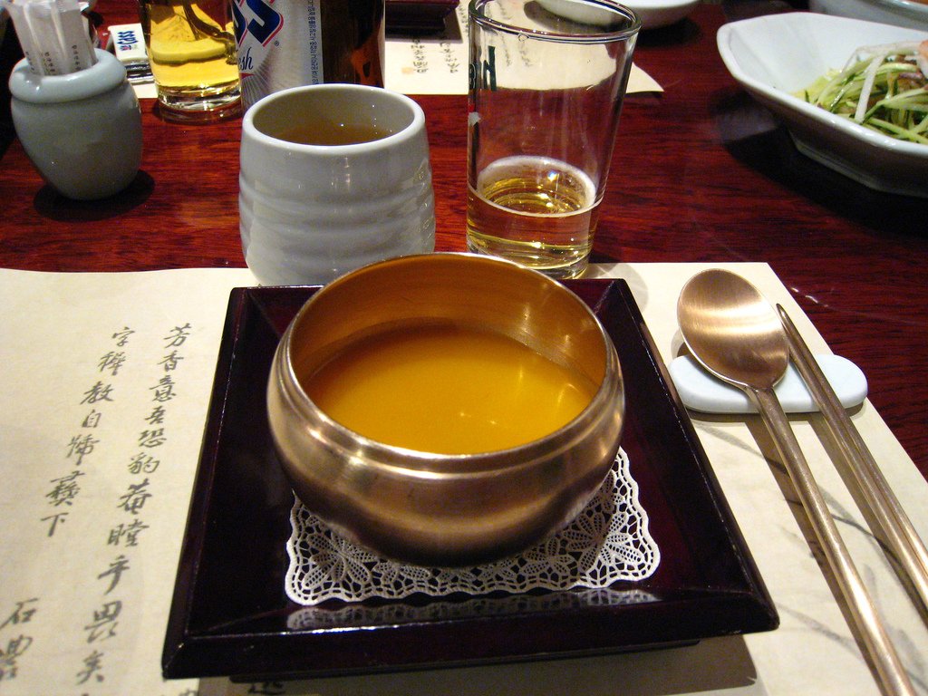 A white bowl of thick orange pumpkin porridge topped with small white rice dumplings
