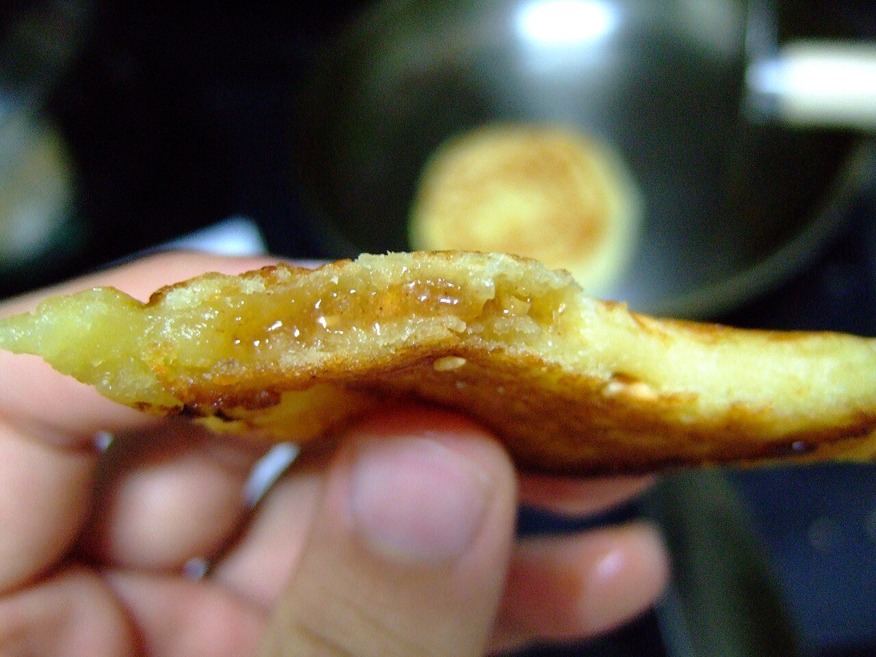 A hotteok torn open to show the dark melted sugar filling inside the soft dough.