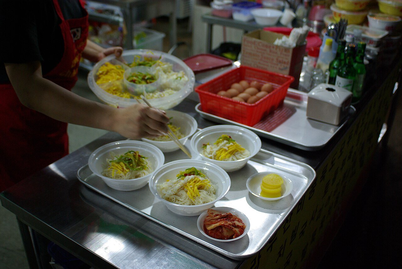 A close-up bowl of janchi guksu with julienned egg, zucchini, and gim on top of noodles in broth