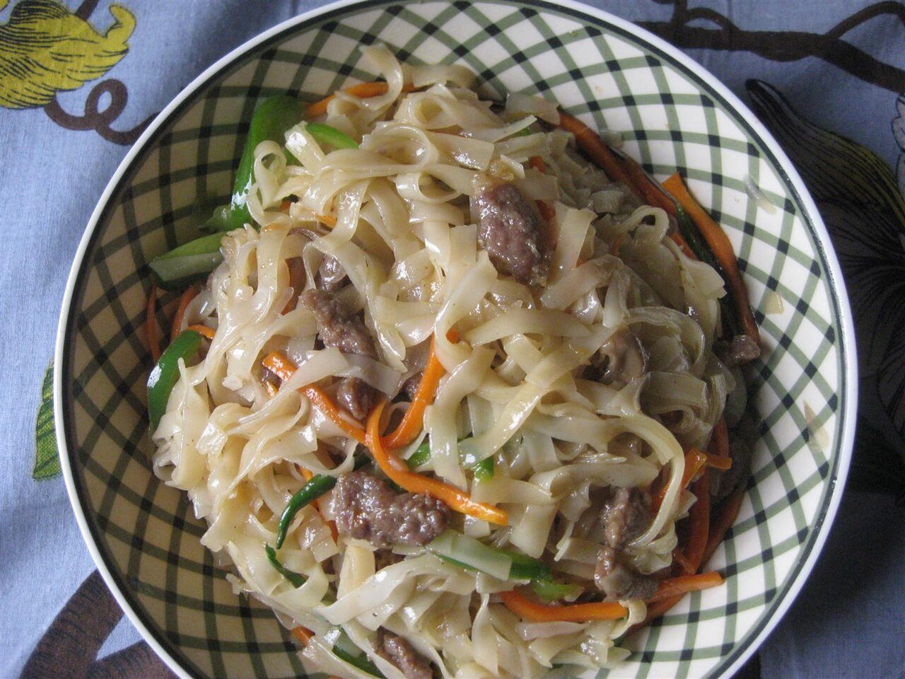 Japchae in a bowl showing distinct strands of orange carrot, red pepper, dark mushroom and green vegetable mixed through the noodles