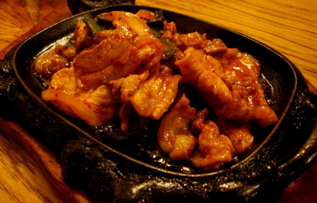 A skillet of jeyuk bokkeum, thin-sliced pork stir-fried in a thick red gochujang sauce with onion