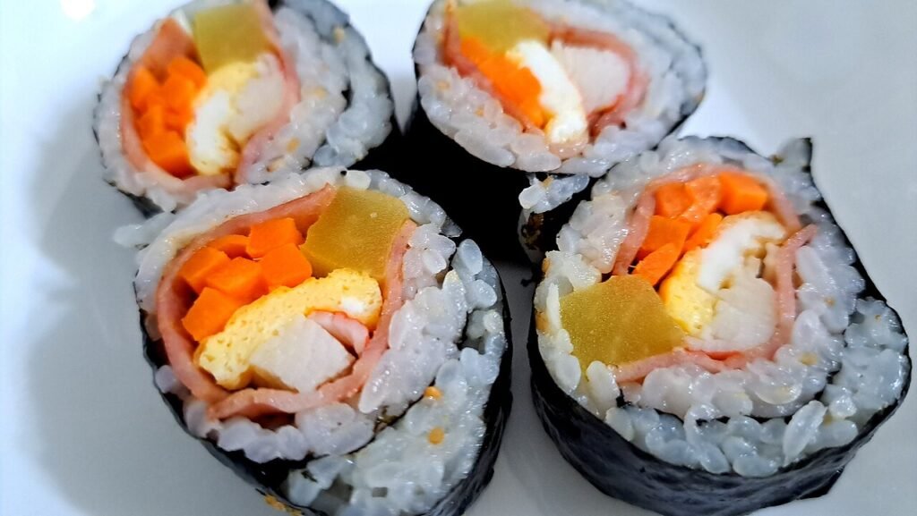 A plate of sliced kimbap rolls showing stripes of egg, carrot, pickled radish and spinach in each round