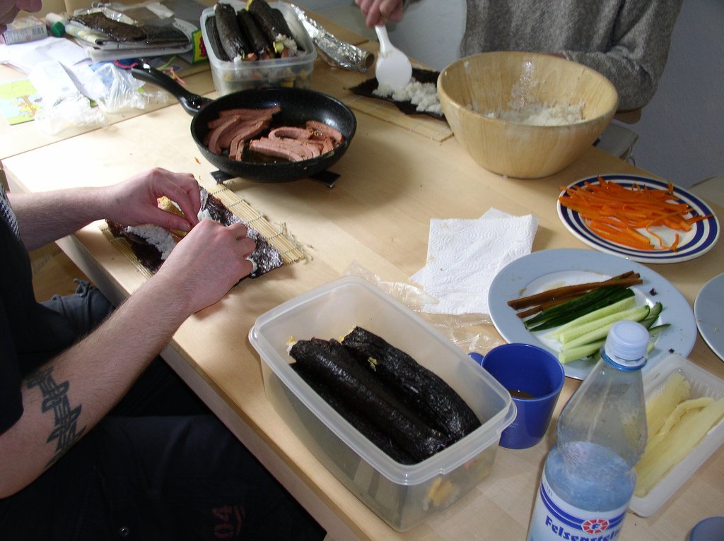 Hands rolling a sheet of seaweed and rice over a line of fillings on a bamboo mat