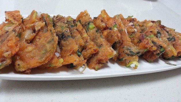 Two kimchi pancakes stacked on a plate, edges dark and crisped from frying