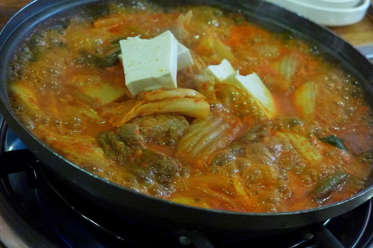 A bubbling pot of red kimchi stew with pork and scallions, served with rice