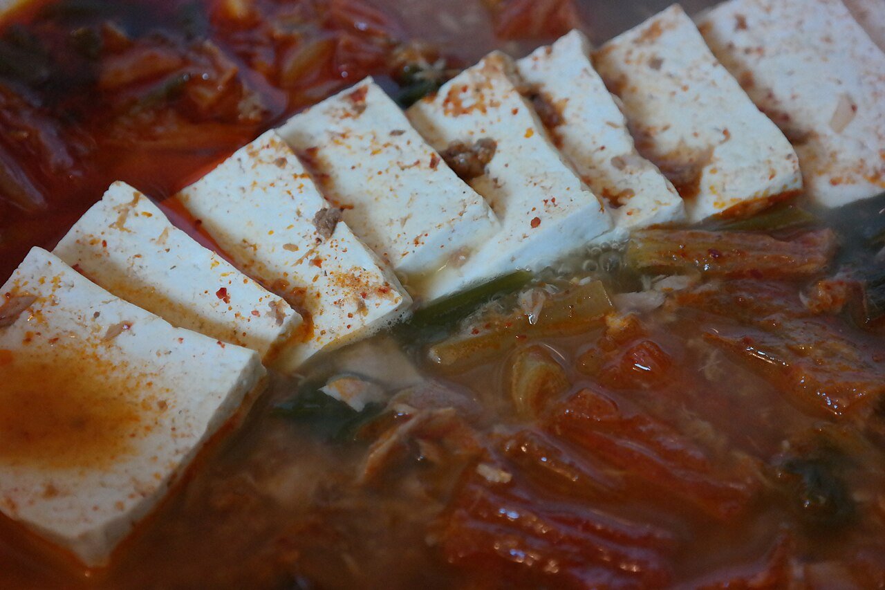 Kimchi stew in a shallow pot with slices of soft tofu laid across the surface