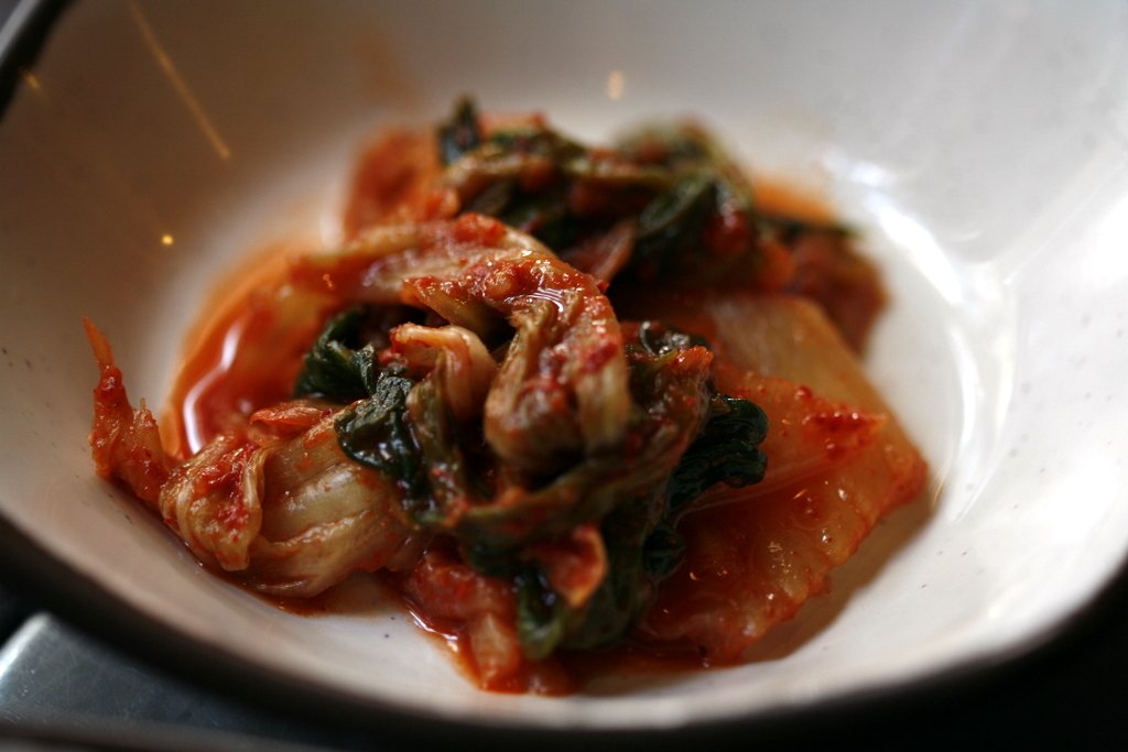 Napa cabbage kimchi in a white bowl, leaves coated in red seasoning