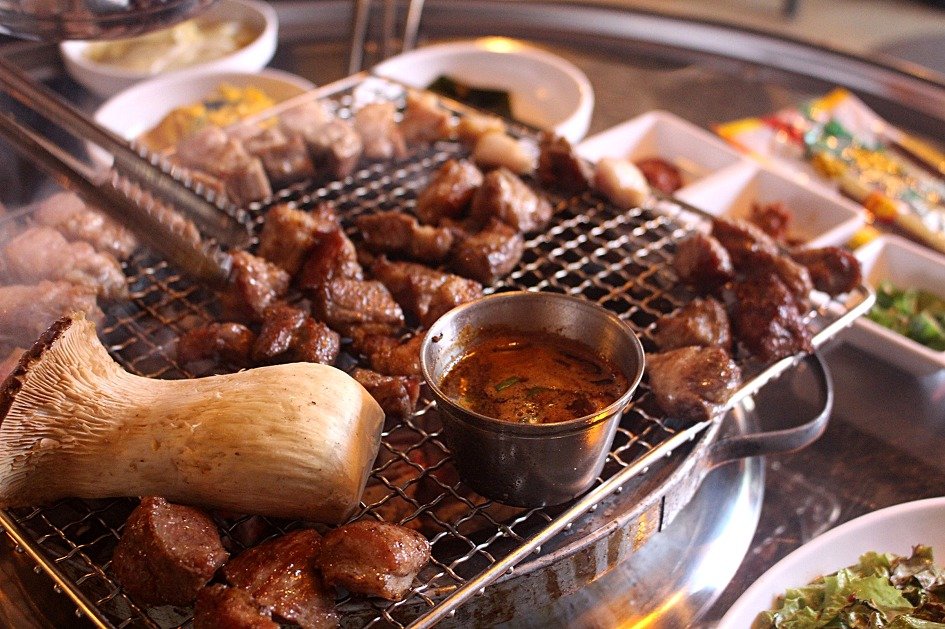Pork collar, pork belly and mushrooms grilling together on a Korean barbecue gridiron at a tabletop grill