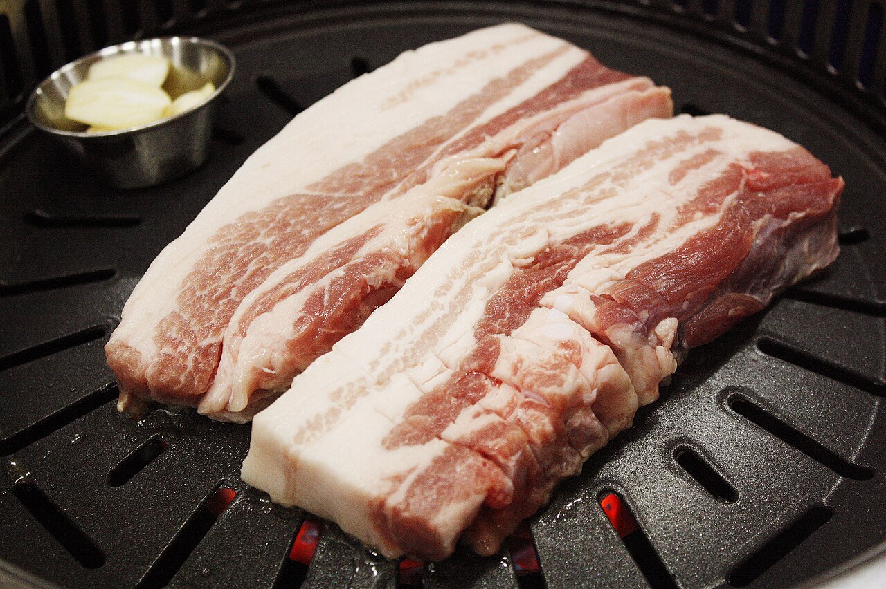 Thick slices of raw pork belly laid out on a plate, ready for grilling