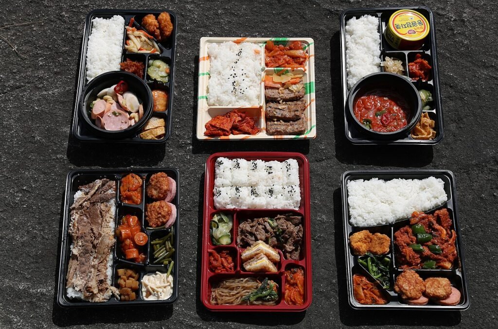 An open Korean convenience store lunch box with rice, fried side dishes and pickled vegetables in separate compartments