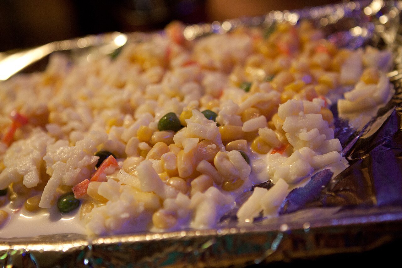 Close-up of corn cheese in a small cast iron pan, cheese bubbling at the edges