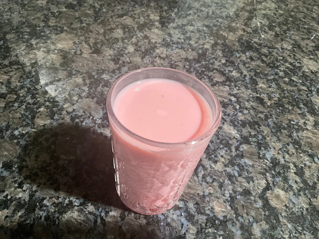 A glass cup filled with pale pink strawberry milk
