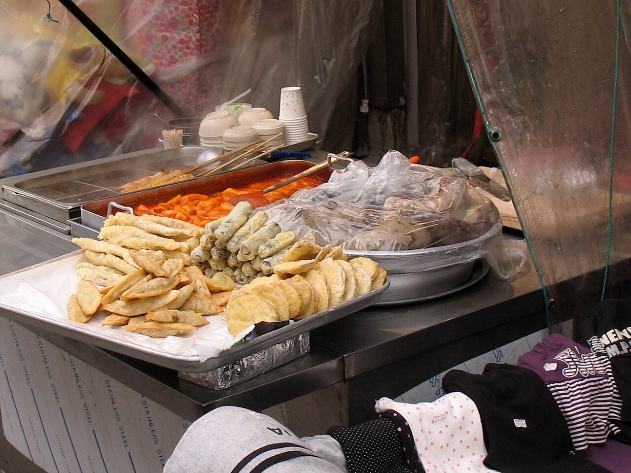 A Korean street food stall display case with fritters, rice cakes and fish cake skewers