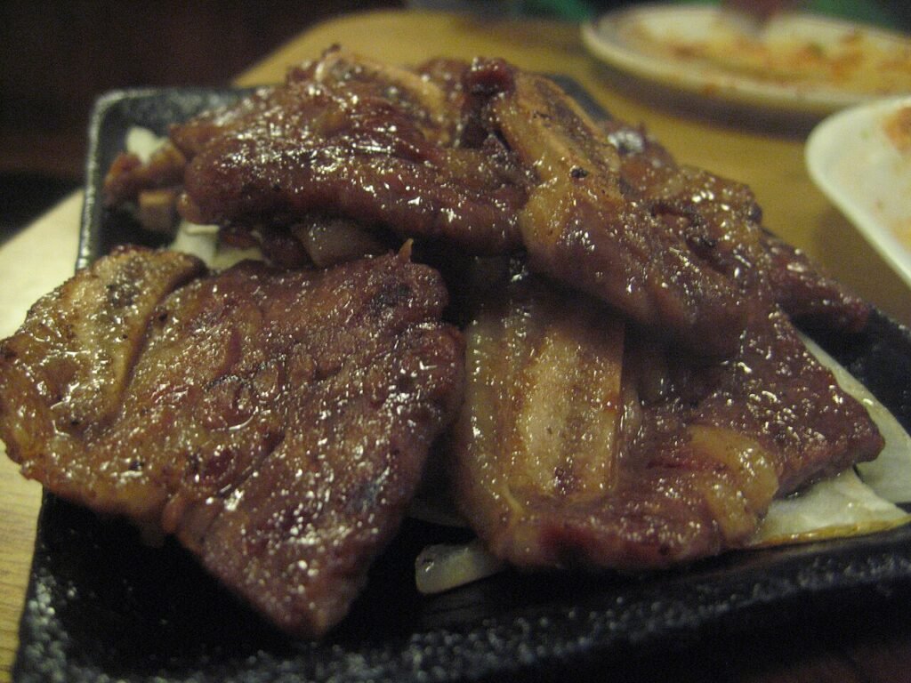 Marinated LA galbi short ribs grilling over charcoal, cross-cut bones visible in each strip
