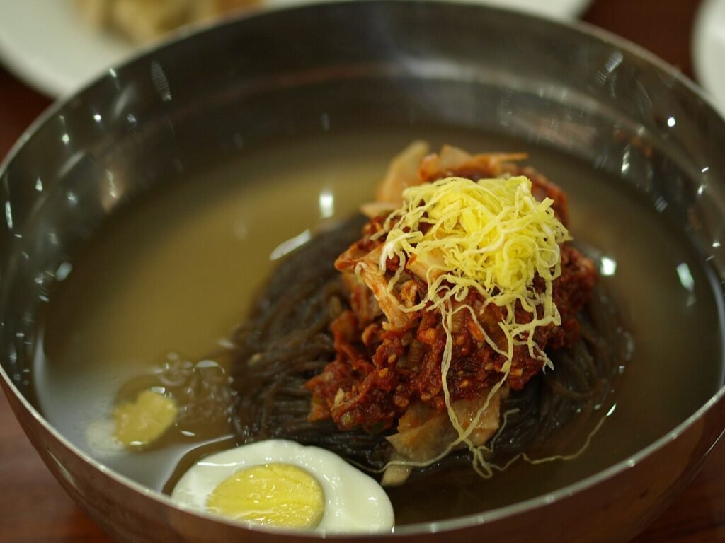 A bowl of mul-naengmyeon, thin buckwheat noodles in cold broth topped with cucumber, egg, and pear slices
