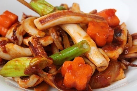 Close view of stir-fried squid pieces in red sauce with onion and scallion