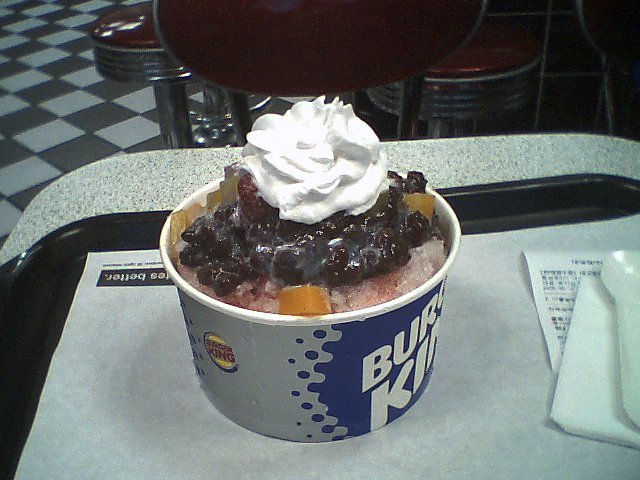 A tall glass of Korean shaved ice dessert with visible layers of red bean and toppings