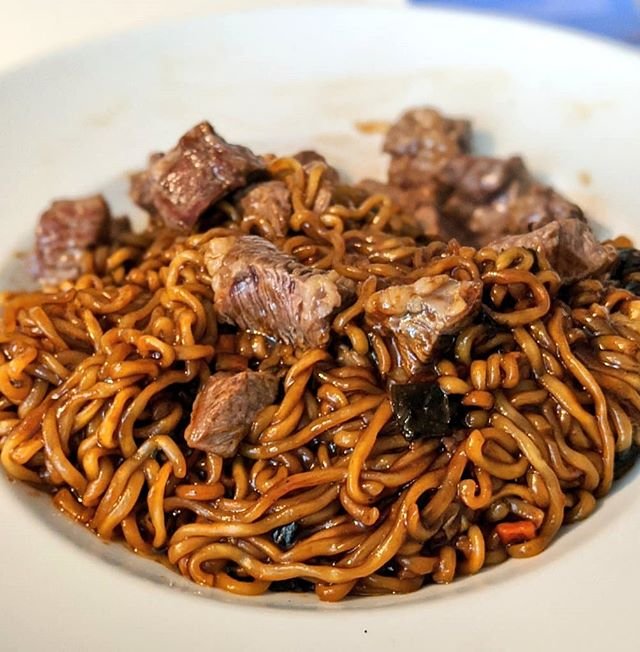 A bowl of ram-don, dark black bean noodles topped with cubes of seared beef